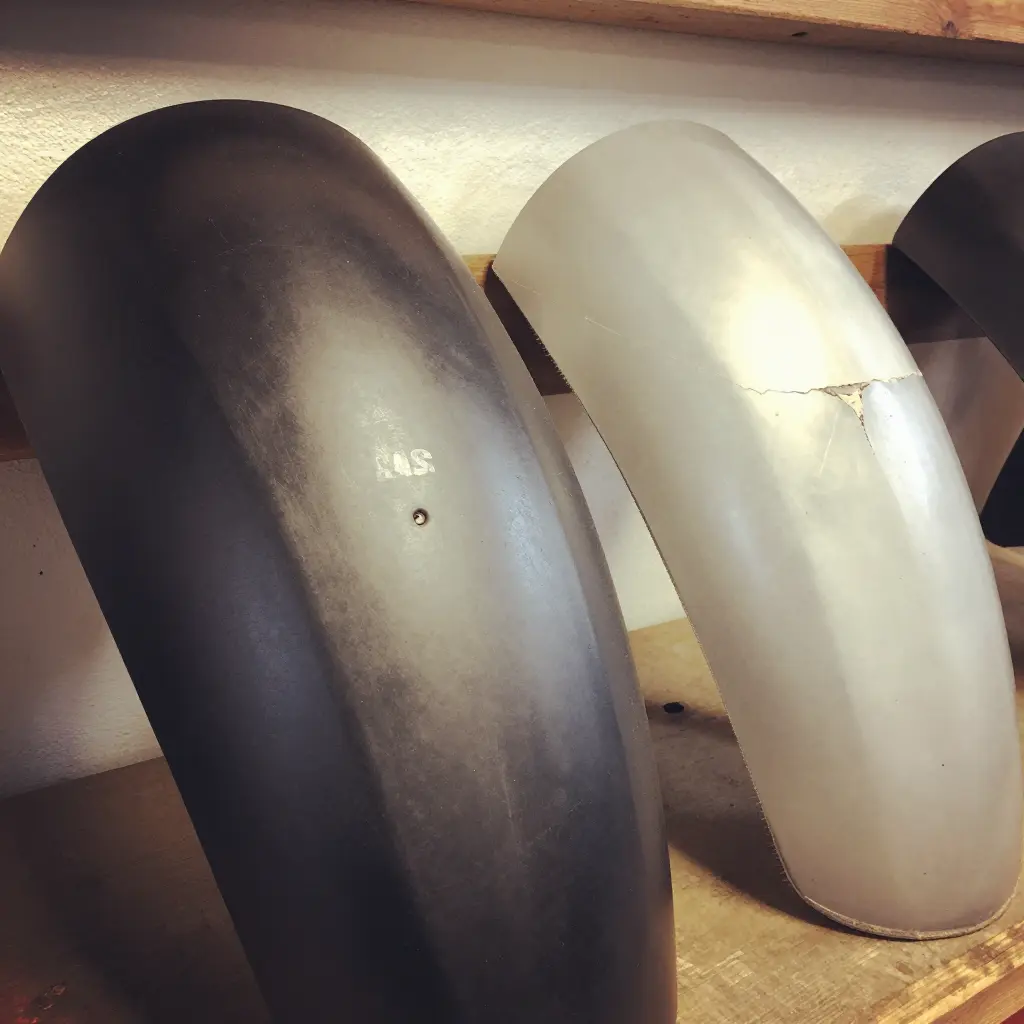 Close-up of a scuffed ABS fairing beside a fiberglass fairing with cracked gel-coat and a chipped edge after real-world riding.